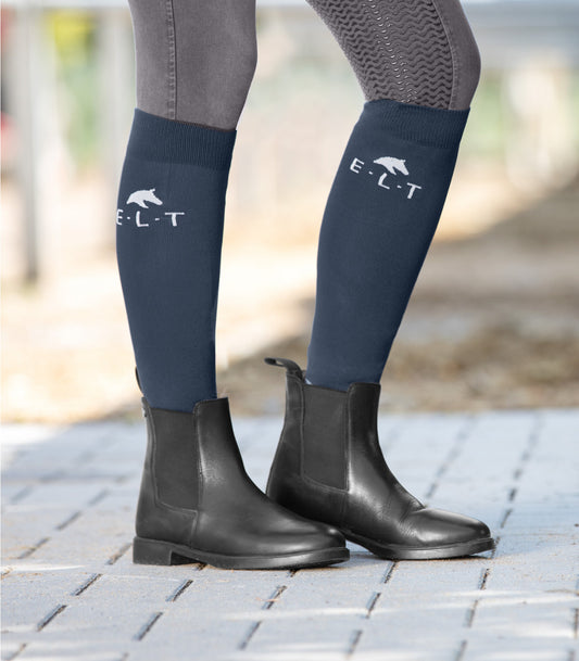 A person wearing navy blue jodhpurs and black classic boots with the logo 'Equestrian' on the upper part.